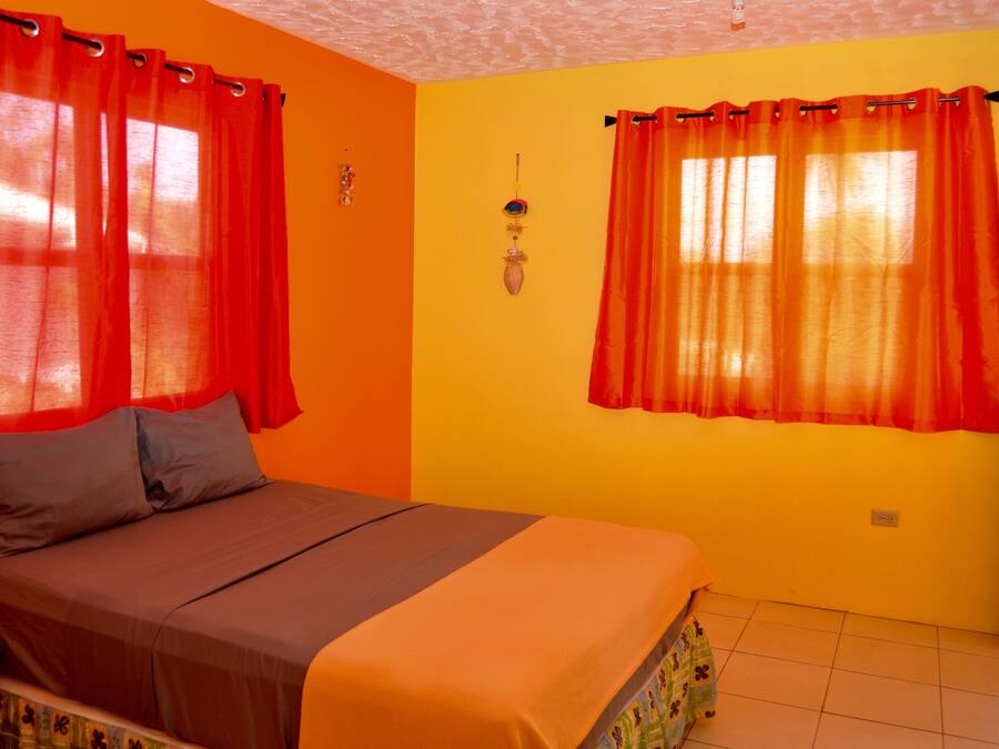 A bedroom with a bed, orange curtains, and a yellow wall.