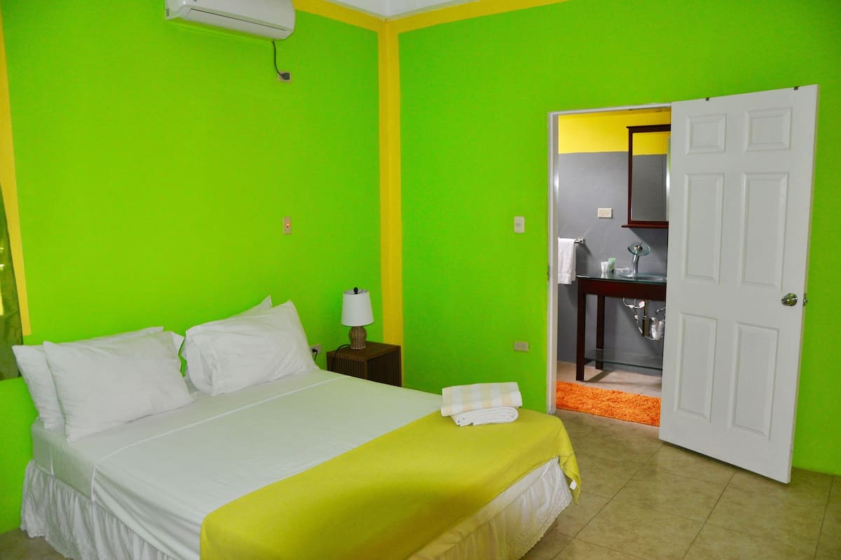 A hotel room with a bed, a nightstand, a lamp, and a bathroom visible through an open door.
