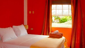 Habitación de hotel con una cama grande, paredes rojas, una ventana con cortinas y un equipo de aire acondicionado.