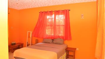 A bedroom with a bed, a nightstand, a mirror, and a window with red curtains.
