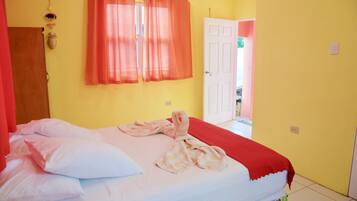 Un dormitorio con cama, almohadas, una manta roja y una ventana con cortinas naranjas.