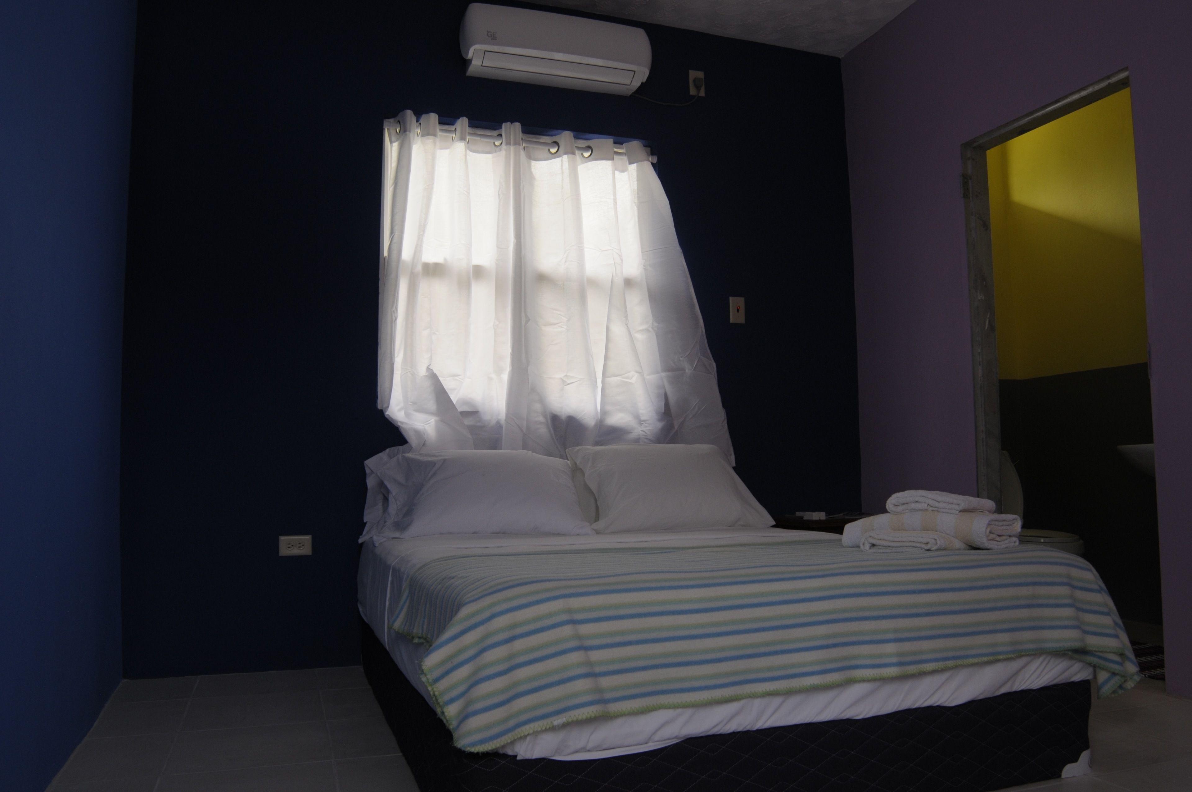A bedroom with a bed, white curtains, a striped bedspread, and a towel on the side.