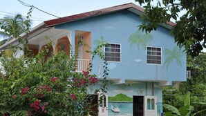 Una casa de dos pisos con un balcón, un acceso con un pequeño porche y un mural de un barco en la pared.