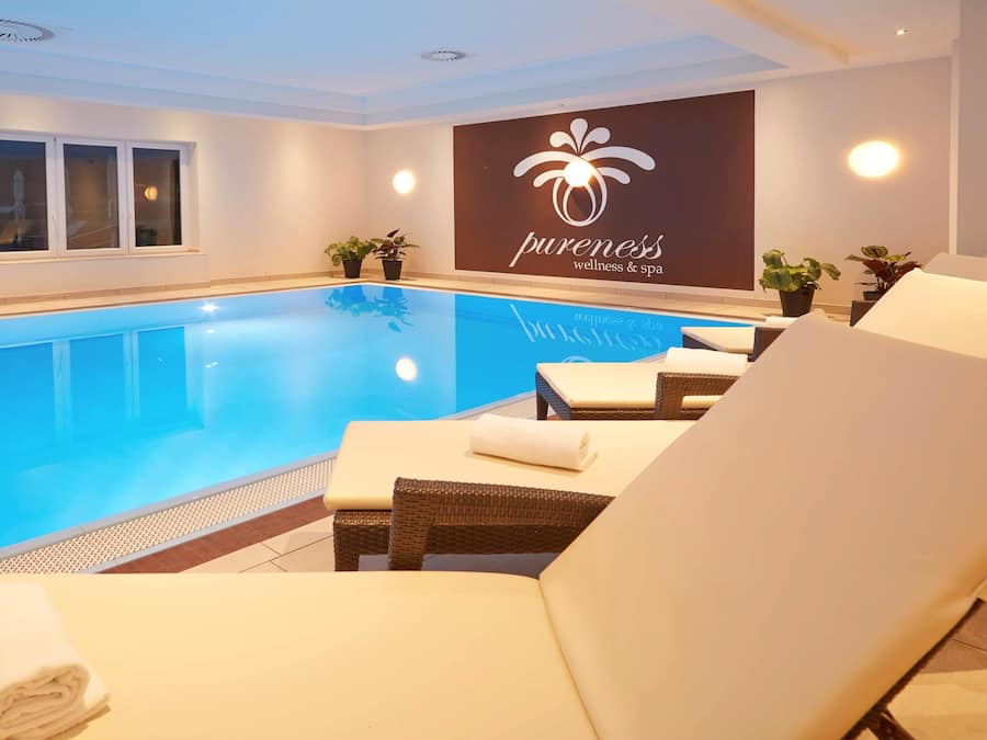 Ein Schwimmbeckenbereich mit Liegestühlen und einer Wand mit dem Logo eines Wellnessbereichs.