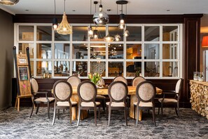 A restaurant with a large window, wooden chairs, a wooden table, and hanging pendant lights.