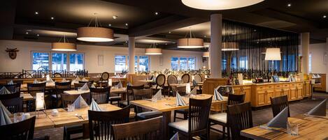A restaurant with multiple dining tables, chairs, and pendant lighting fixtures.