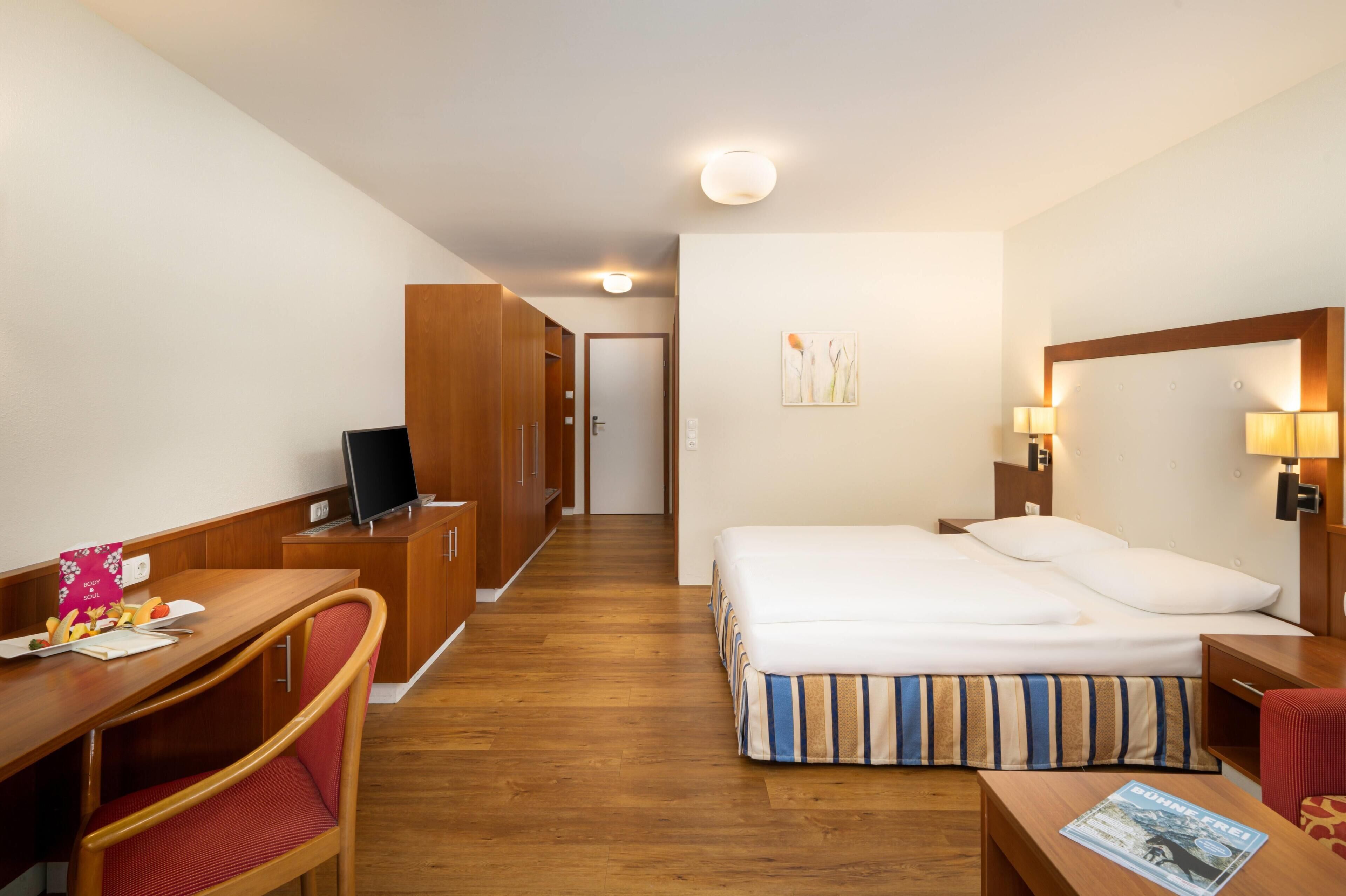 A hotel room with a bed, a desk, a chair, a television, and a wardrobe.