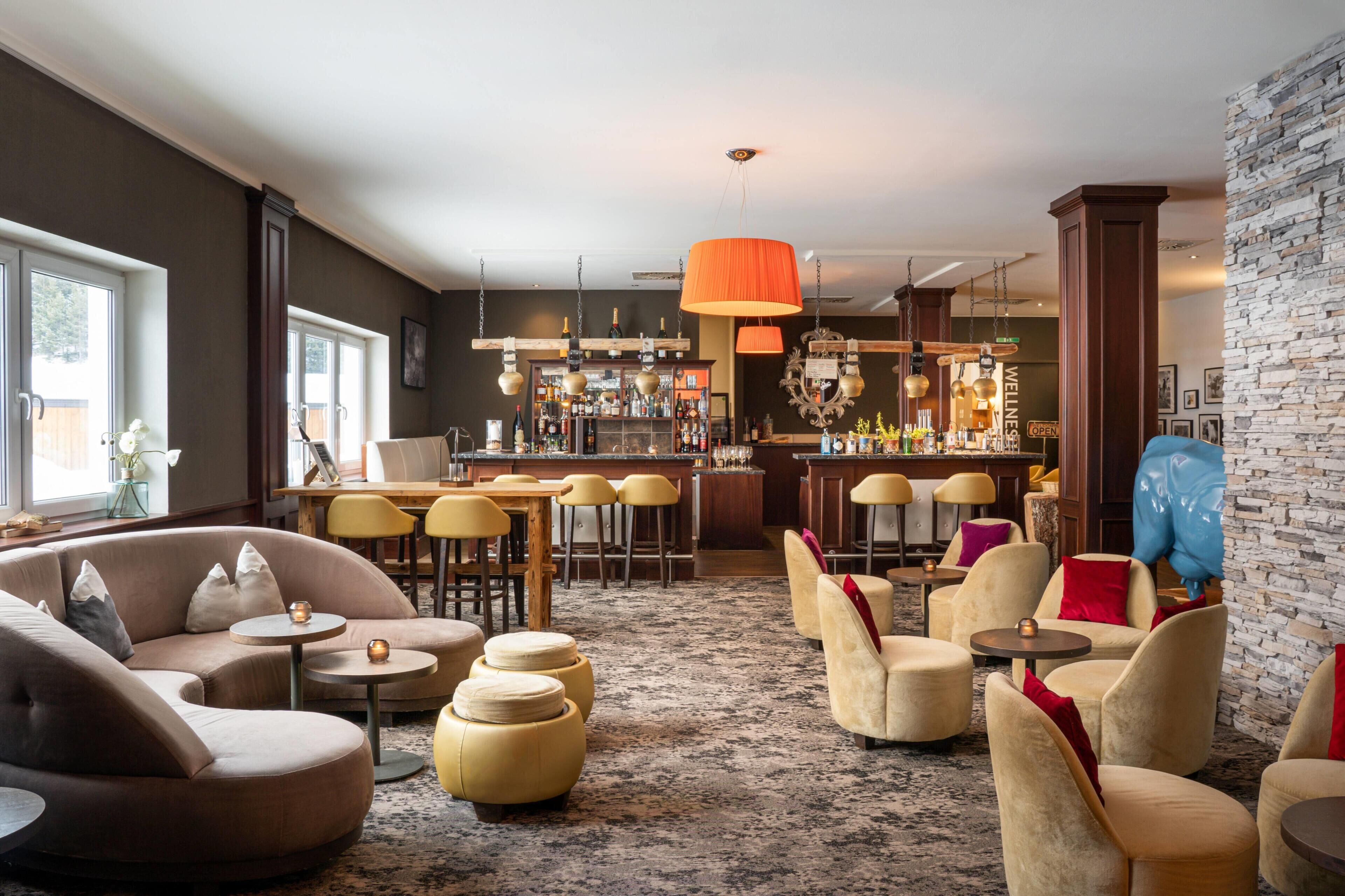 A modern bar area with a stone wall, a bar counter, and seating arrangements including sofas and round tables.
