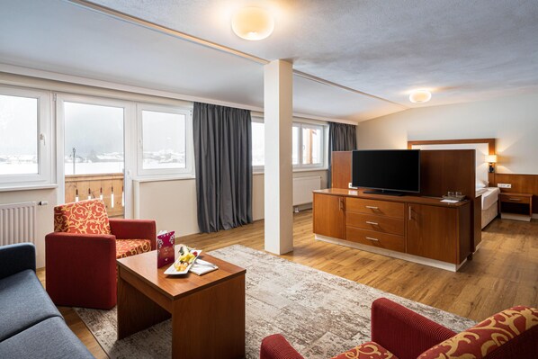 Una habitación de hotel moderna con sofá, televisor, mueble de madera y mesa de comedor con fruta.