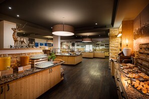 A modern kitchen with wooden cabinets, a central island, and a variety of food items displayed. - KUHOTEL Steinplatte, Trademark Collection by Wyndham (Waidring)