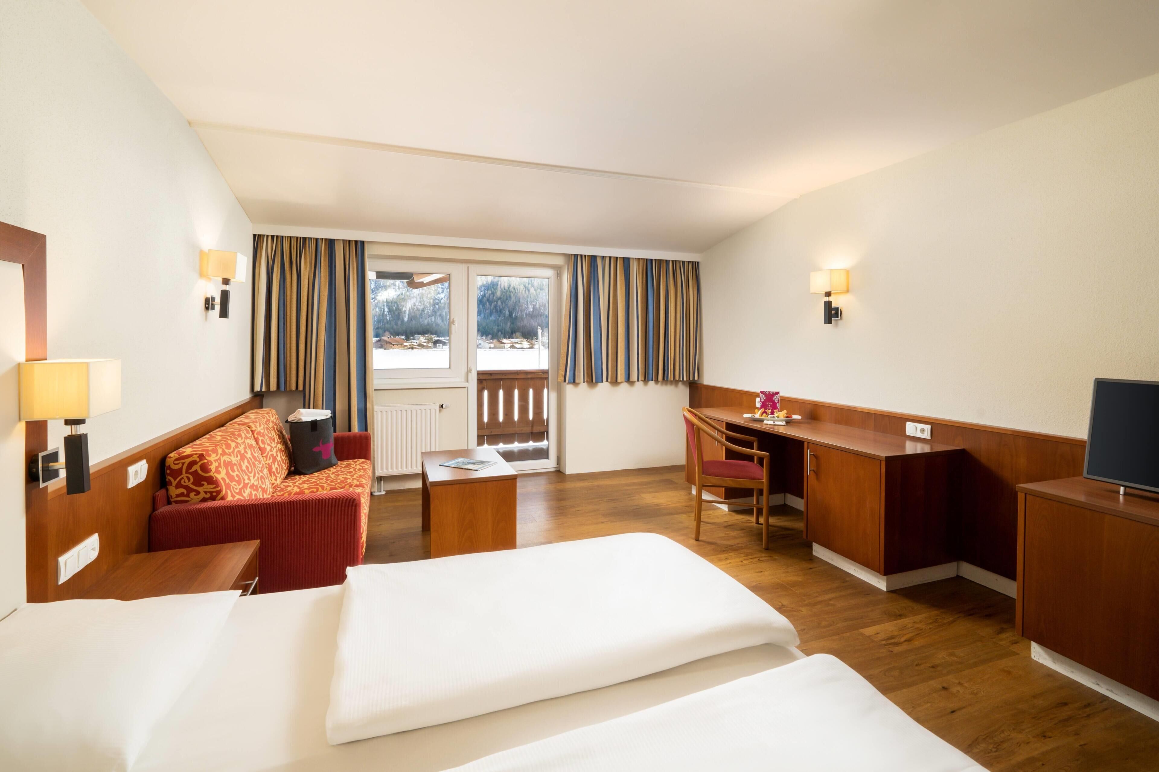 Een hotelkamer met een bed, bureau, stoel, bank en uitzicht op het omliggende landschap.