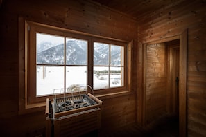 Interior de una cabaña de madera con un amplio ventanal que muestra montañas nevadas.