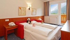 A hotel room with two beds, a red sofa, a panda plush toy, a lamp, and artwork on the wall.
