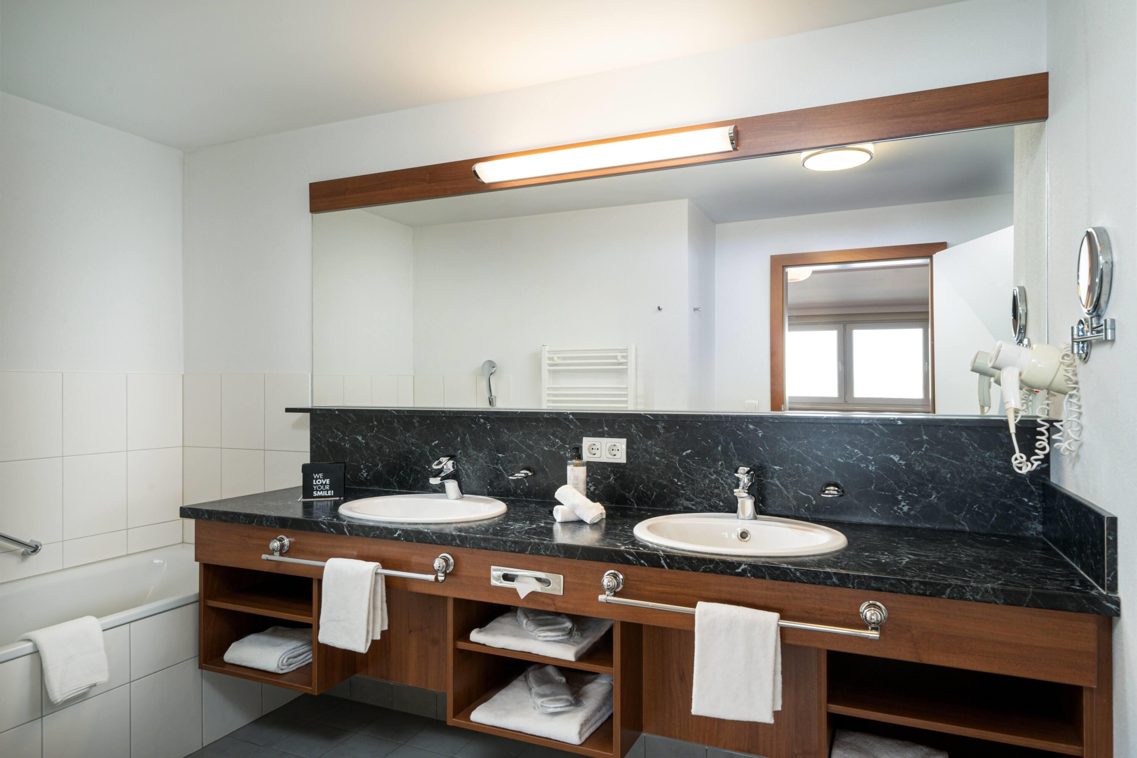 Un baño con dos lavamanos, un espejo grande y un perchero para toallas.