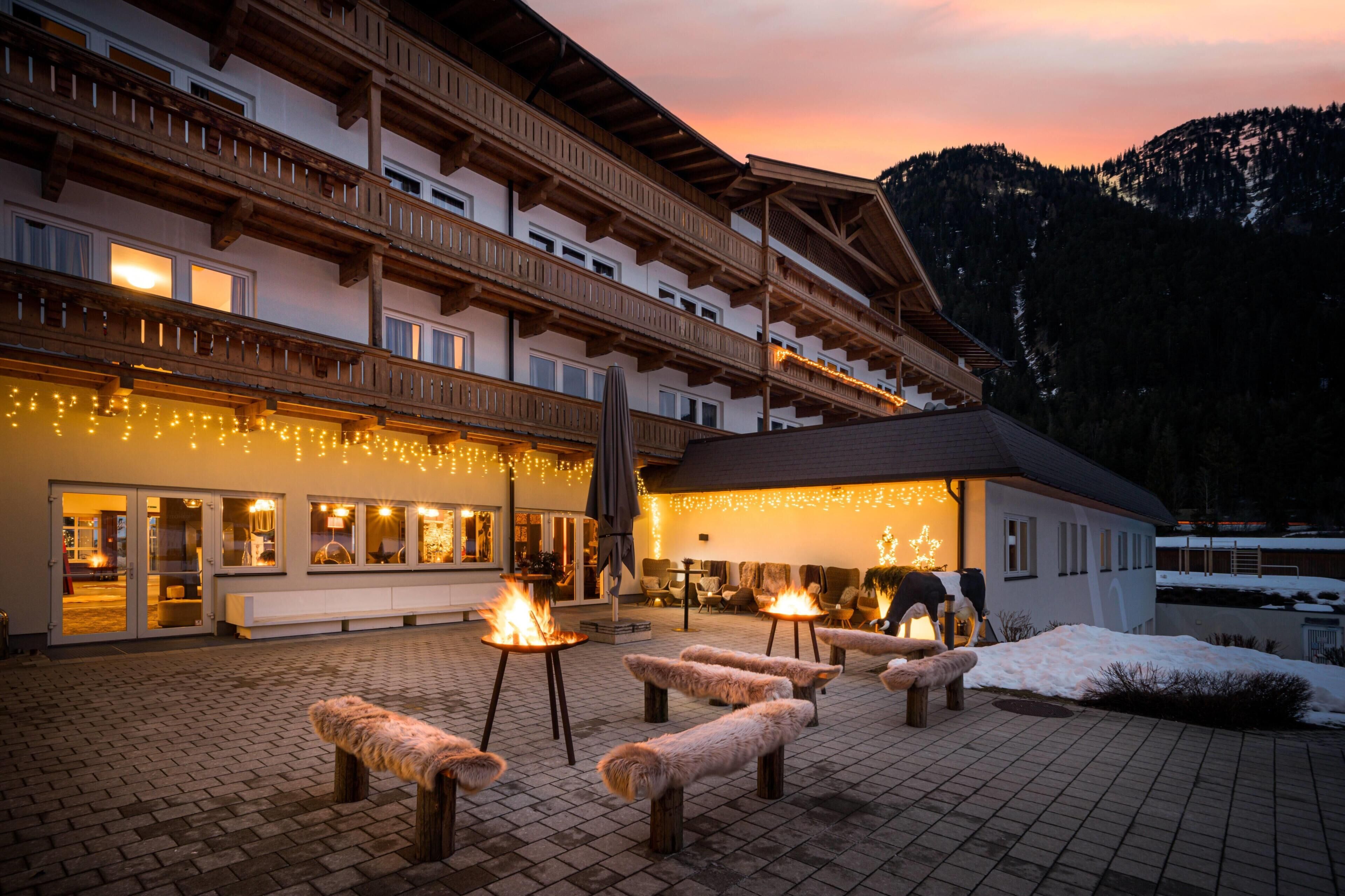 Un hotel con terraza, chimenea y montañas al fondo.