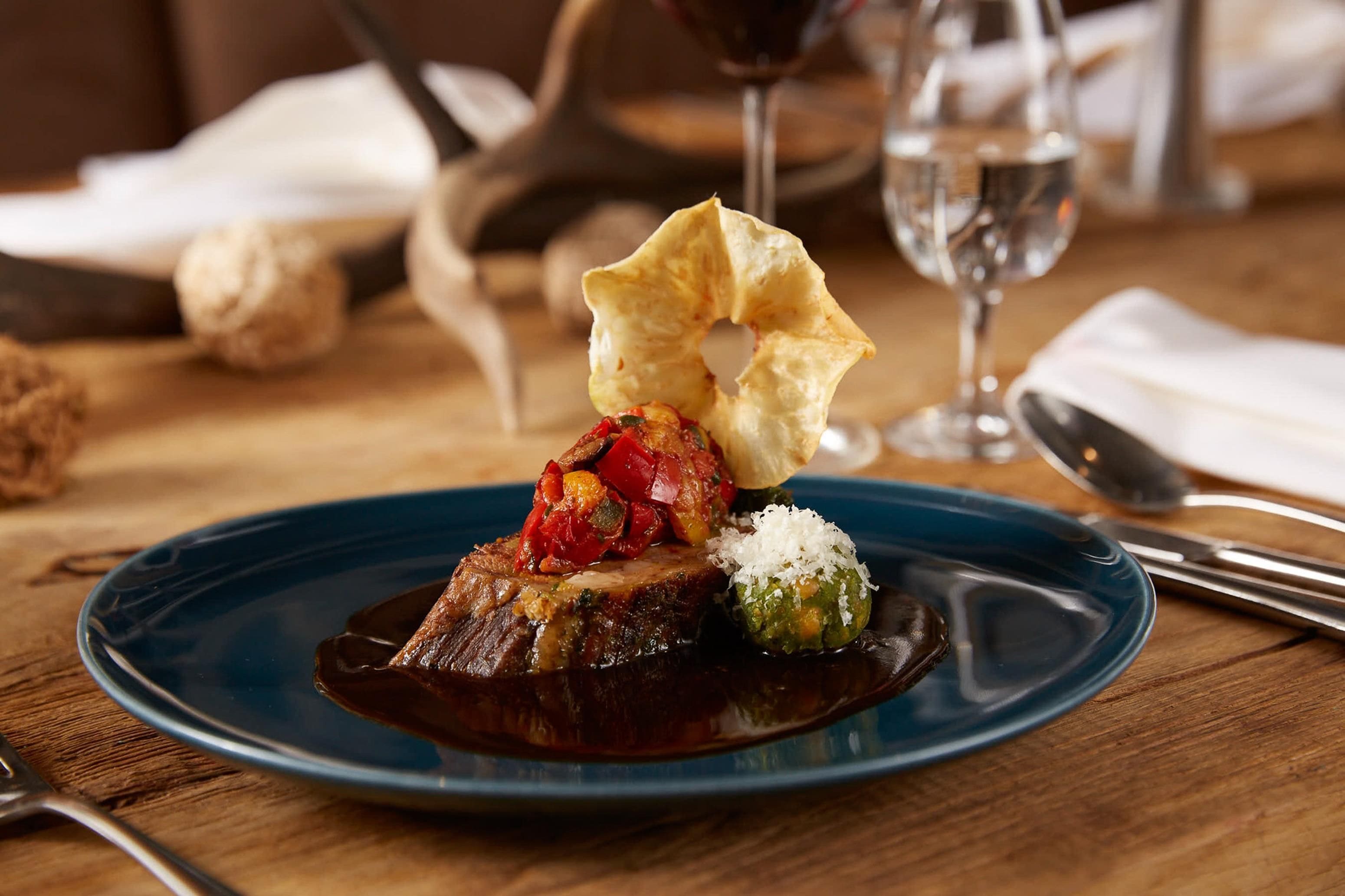 A plate with a steak, a piece of bread, and a small green vegetable on a blue plate.