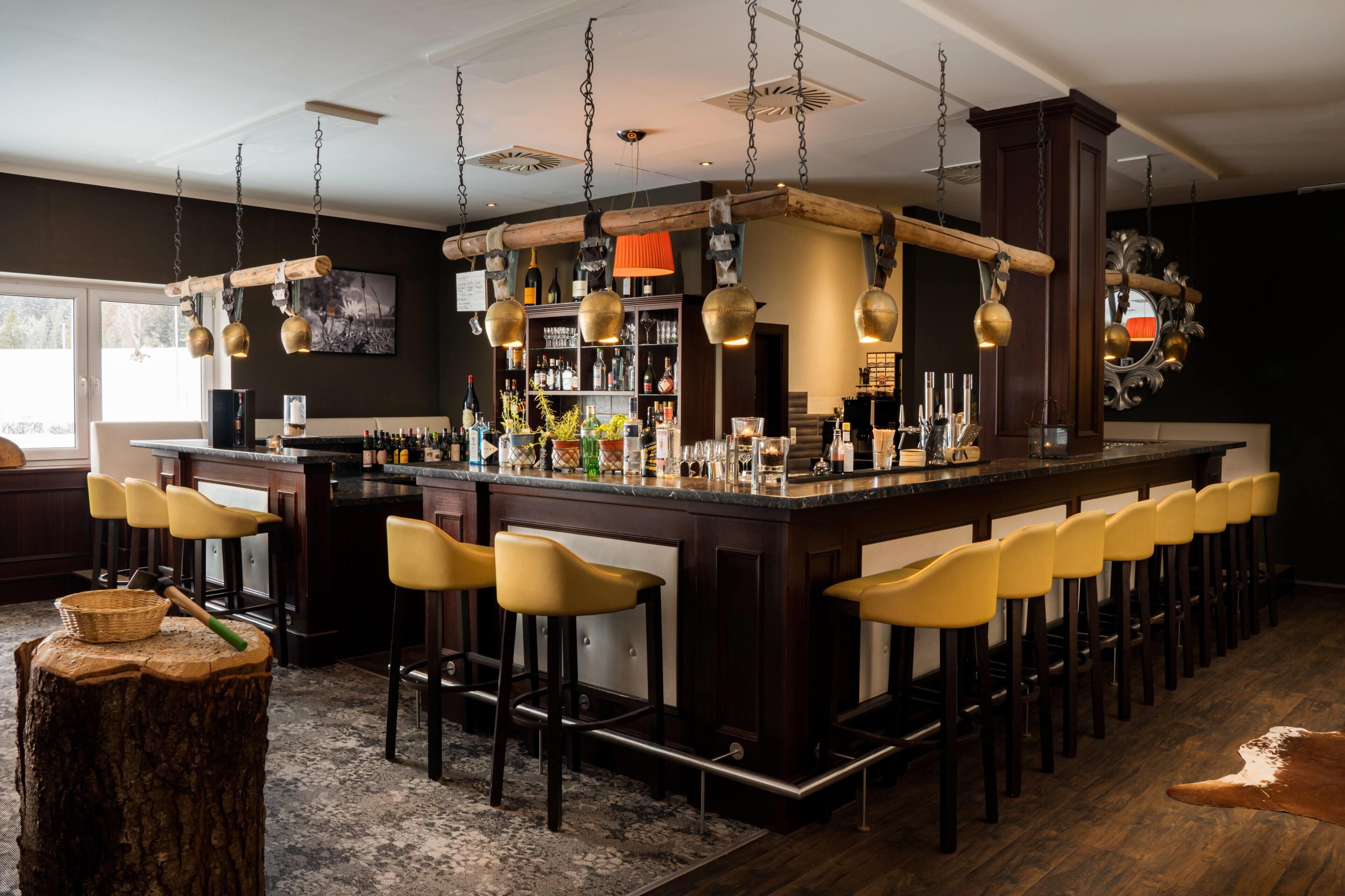 Een bar met een lange toonbank, meerdere krukken, hangende lampen en diverse flessen en glazen.