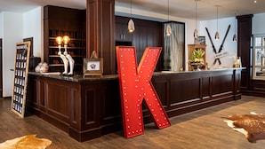 A hotel reception area with a large illuminated 'K' sign, wooden paneling, and a leather hide on the floor. - KUHOTEL Steinplatte, Trademark Collection by Wyndham (Waidring)