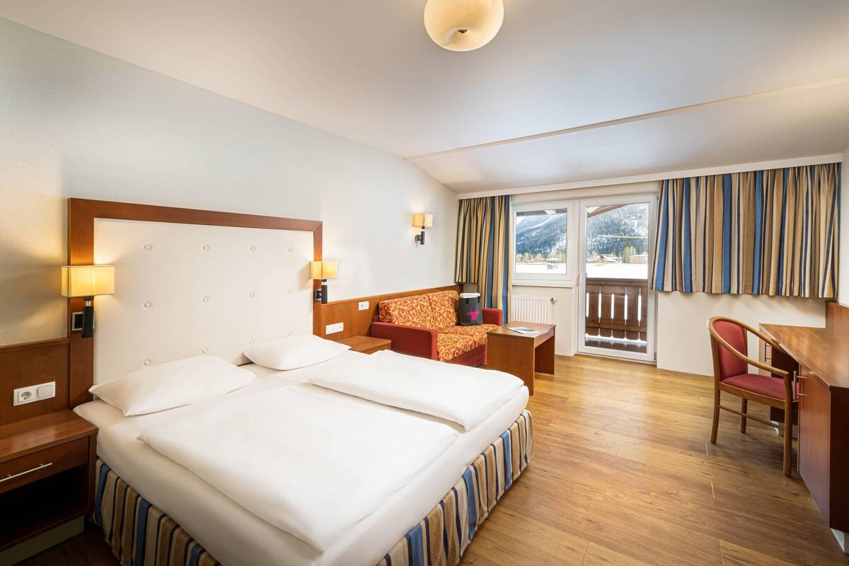 Une chambre d’hôtel avec un grand lit, un bureau, une chaise et une vue sur l’extérieur.
