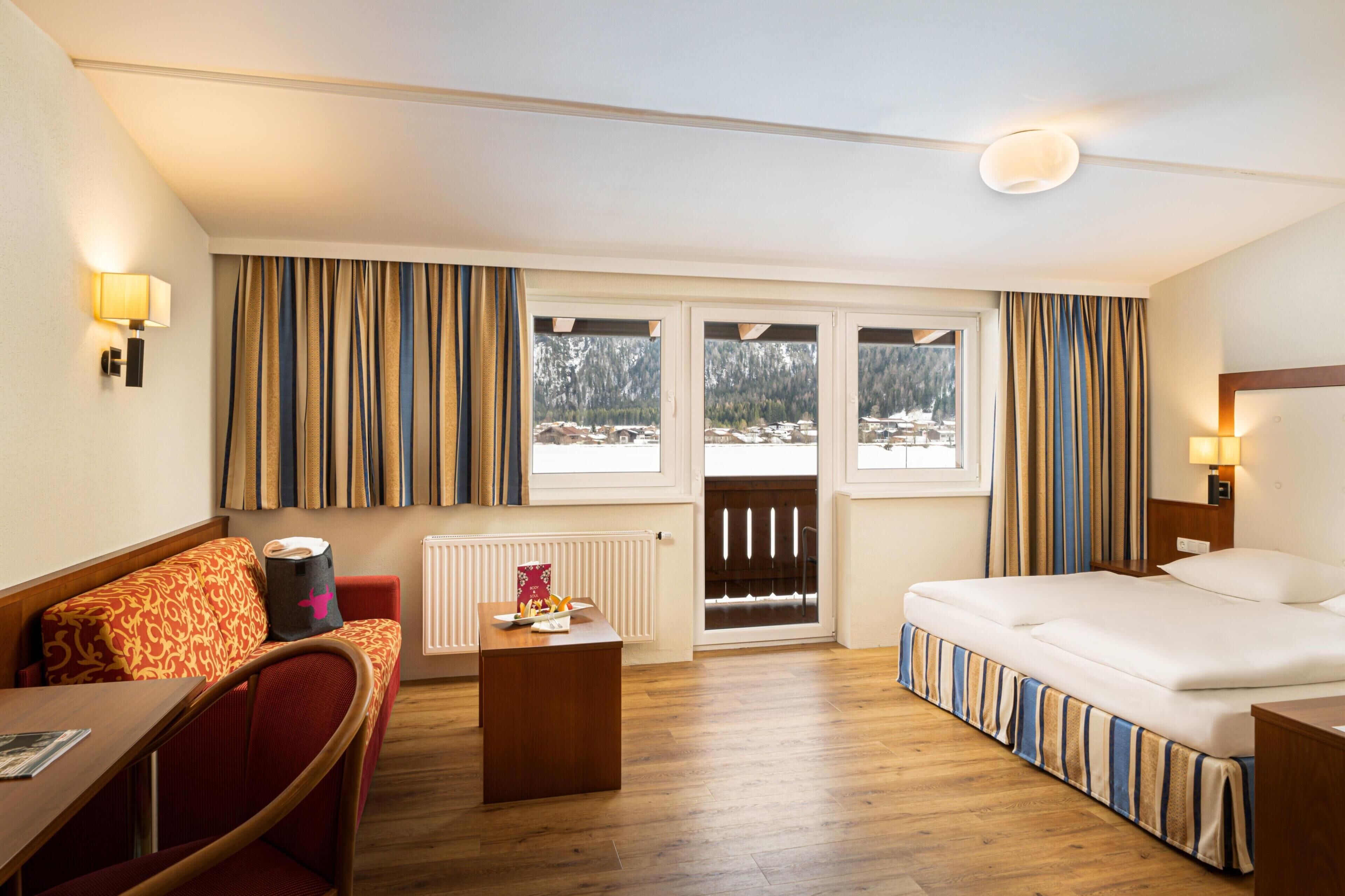 Een hotelkamer met een bed, een bureau, een stoel, een radiator en uitzicht op een besneeuwde berg.