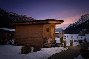 A wooden cabin with a door and windows, surrounded by snow and mountains. - KUHOTEL Steinplatte, Trademark Collection by Wyndham (Waidring)