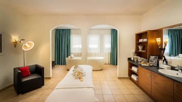 Een hotelkamer met een bed, een sofa, een kaptafel met spiegel, een badkuip en een douche.