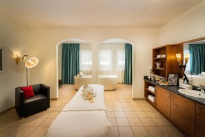 Habitación de hotel con cama, sofá, tocador con espejo, bañera y ducha.