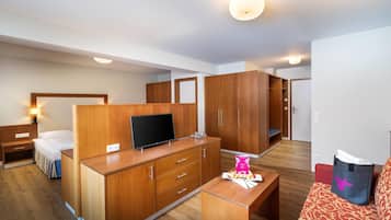 A hotel room with a bed, a TV on a wooden dresser, a desk, and a wardrobe.