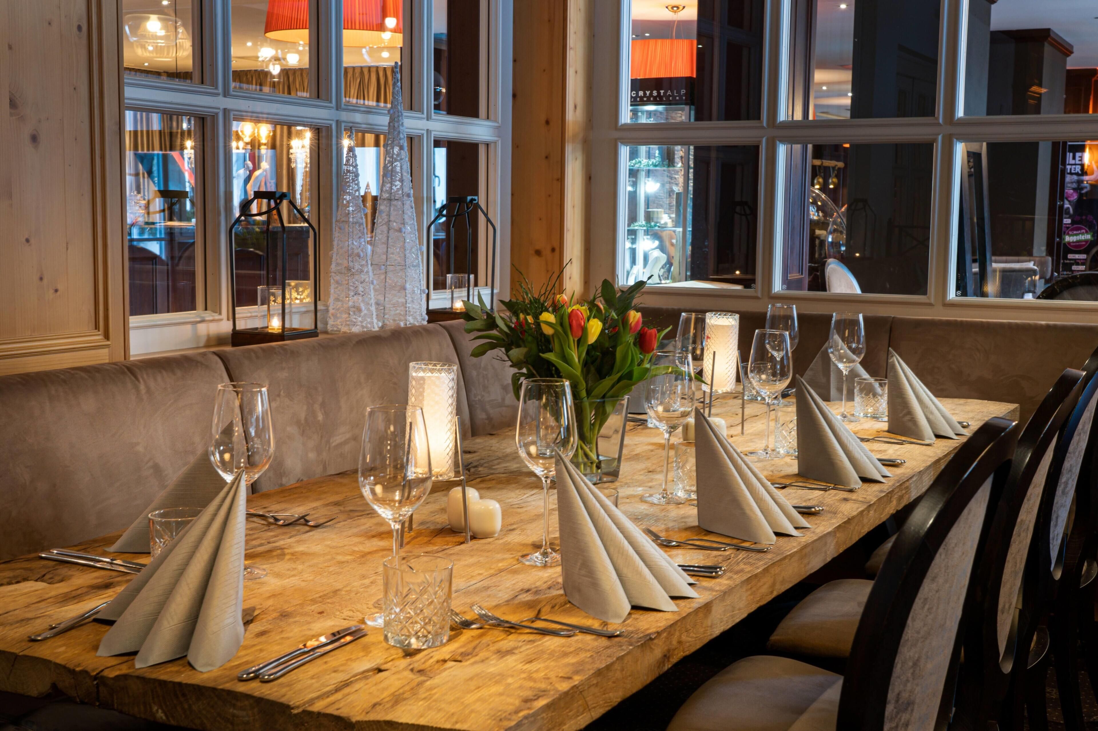 A wooden dining table set with wine glasses, cutlery, and a candle centerpiece.