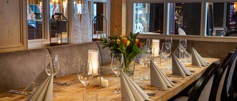 A wooden dining table set with wine glasses, cutlery, and a candle centerpiece.