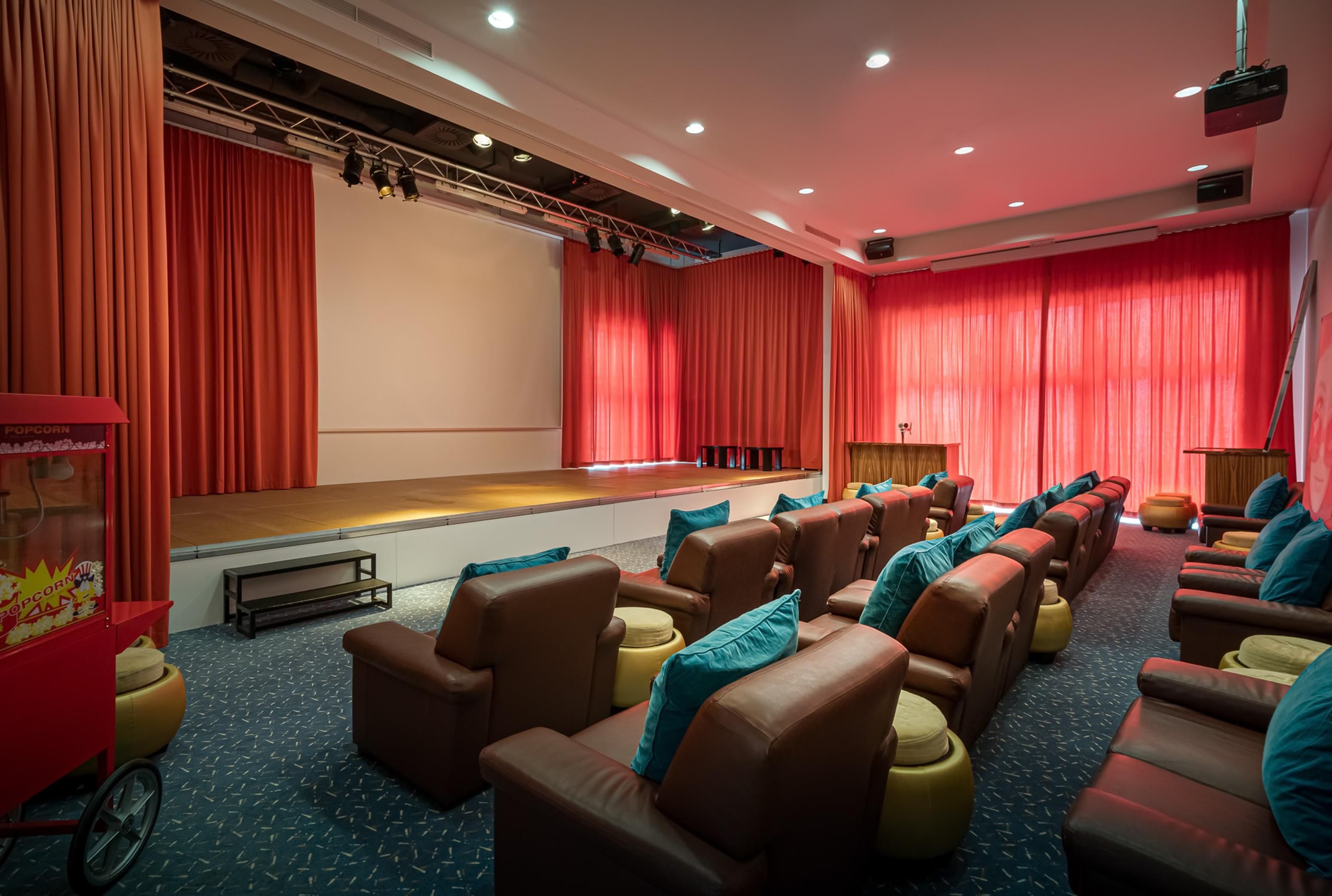 A theater room with rows of leather chairs, a stage with curtains, and a popcorn machine.