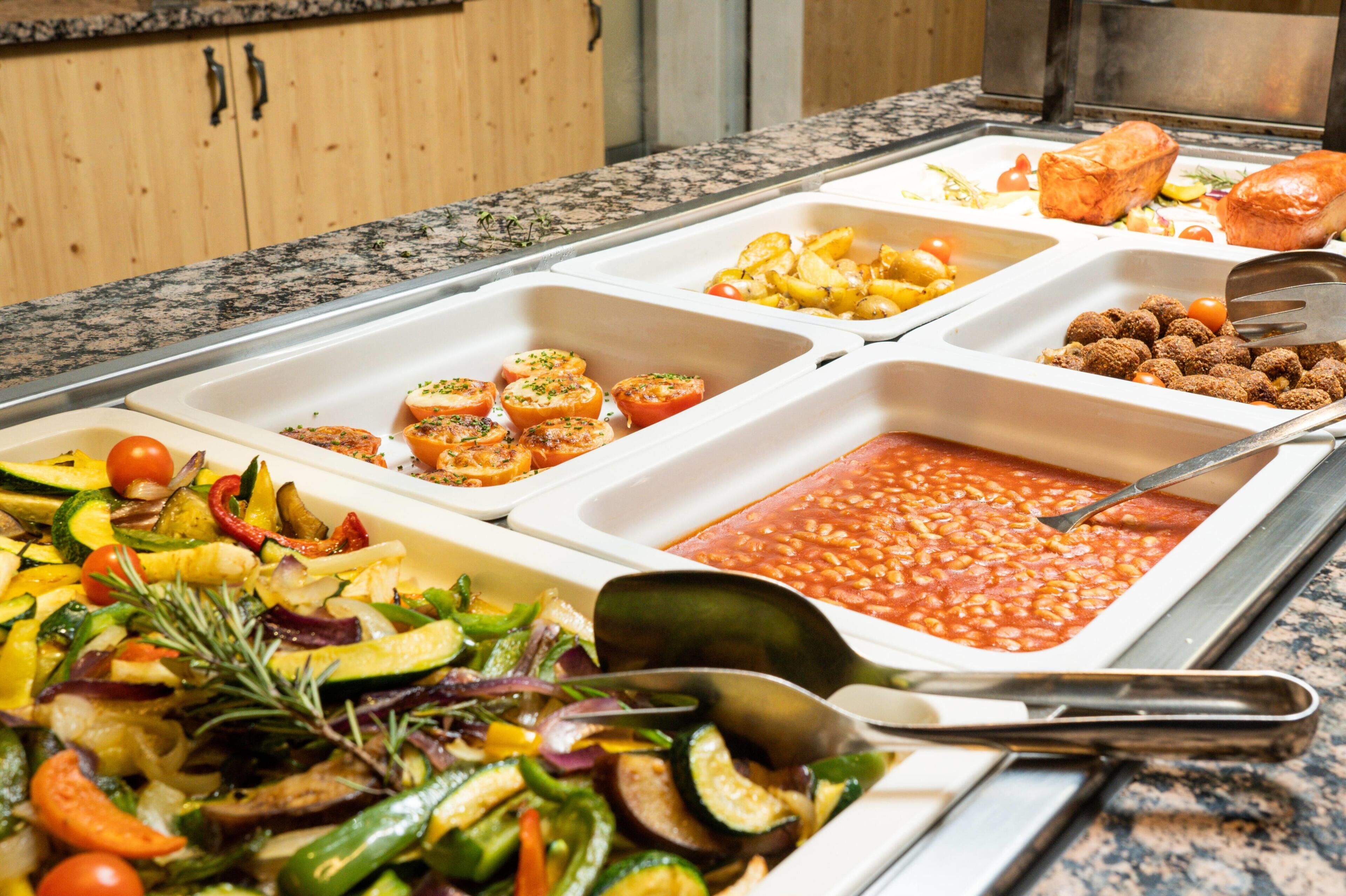 A buffet with various dishes including vegetables, baked goods, and a bean salad.