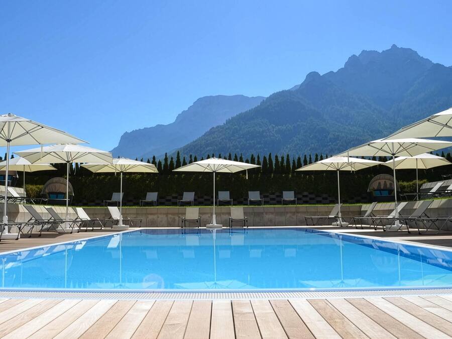A swimming pool with lounge chairs and umbrellas, surrounded by a wooden deck and a mountain backdrop.