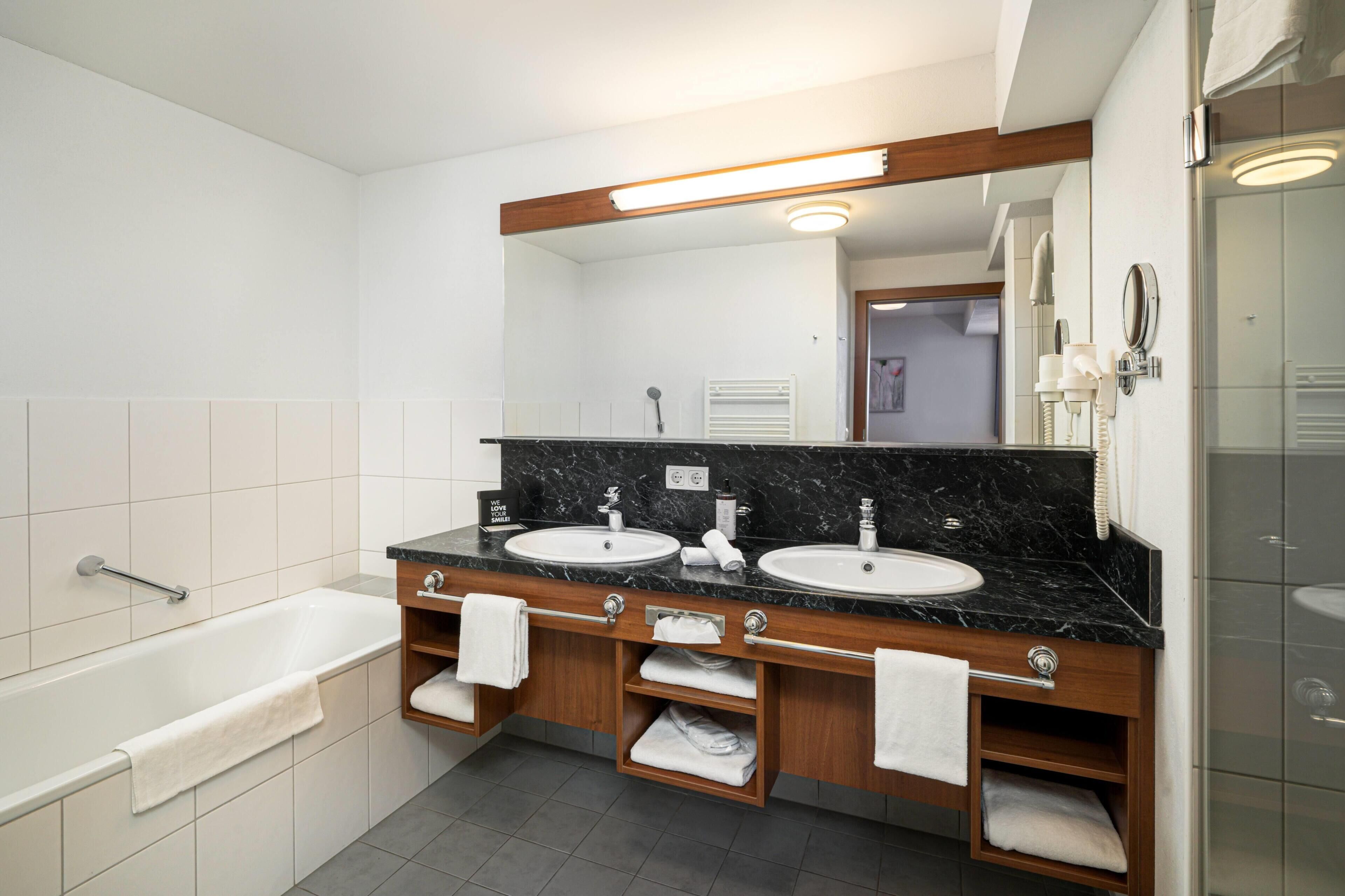 Un baño moderno con dos lavamanos, una bañera y una ducha.