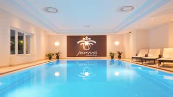 A modern indoor pool area with a clear blue pool, lounge chairs, and a wall with a wellness spa logo.