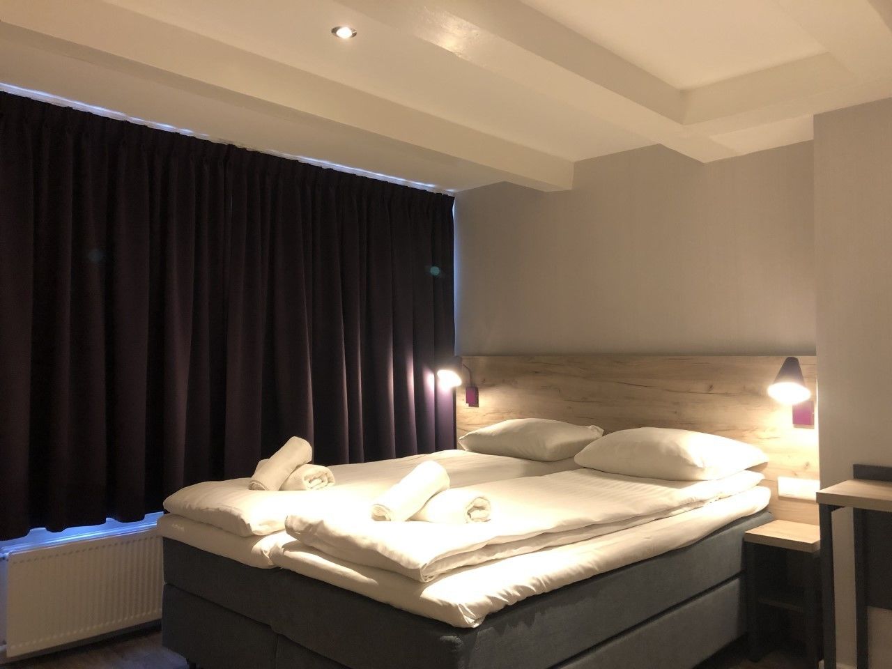 Une chambre d’hôtel avec un grand lit, des rideaux épais, une tête de lit en bois et des lampes de chevet.