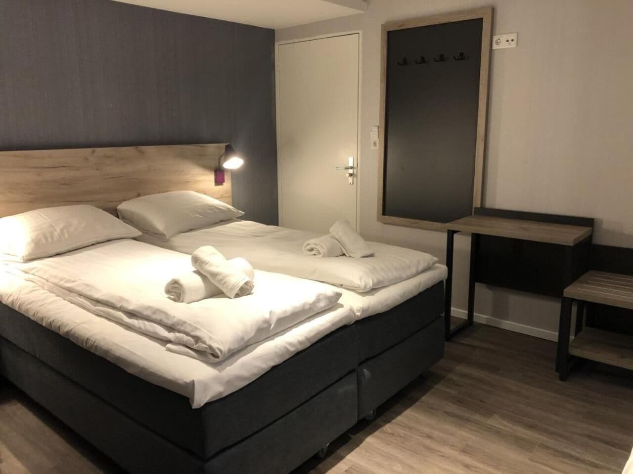 A modern hotel room with a large bed, a bedside table, and a mirror.