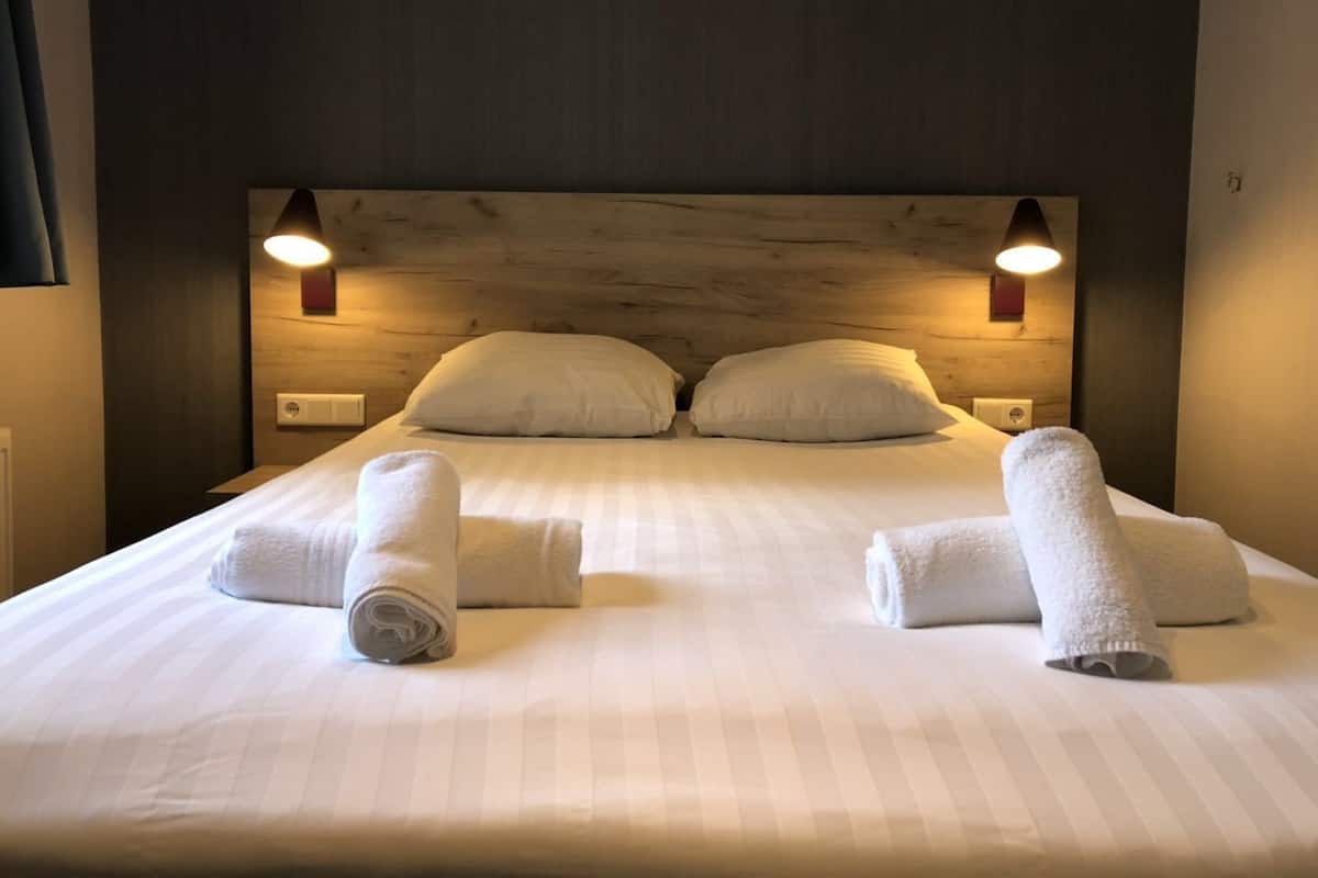 A neatly made bed with two pillows and two rolled towels placed on the bed.