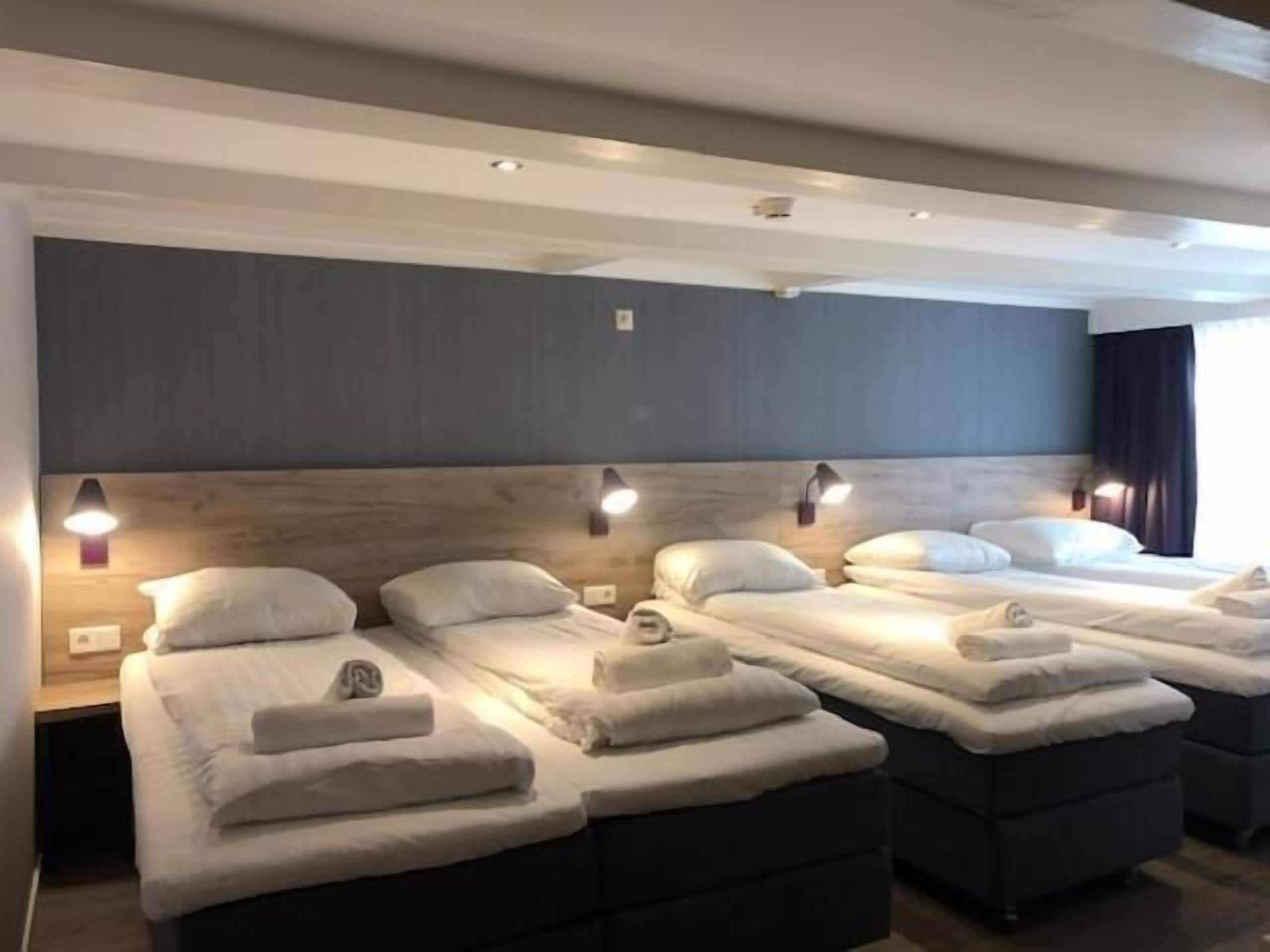 Quarto de hotel com três camas dispostas em linha, cada uma com cabeceira e abajures.