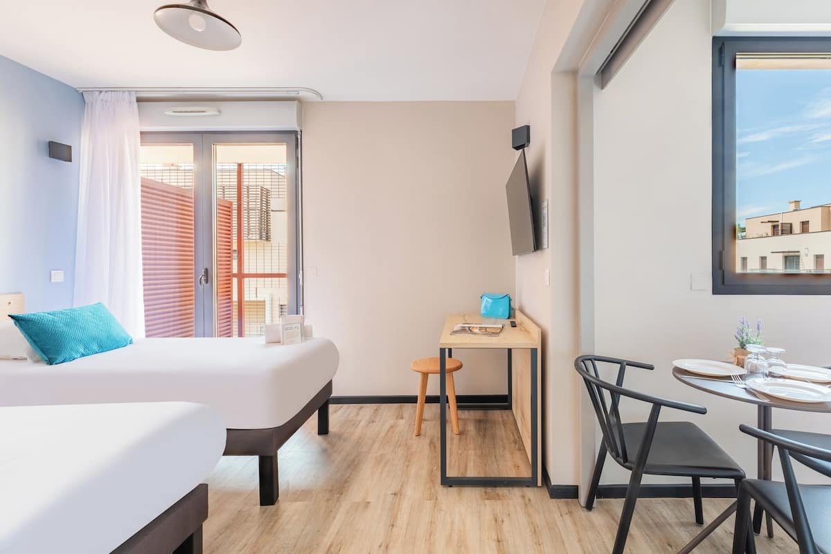 A modern hotel room with a bed, a desk, and a dining area.
