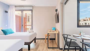 A modern hotel room with a bed, a desk, and a dining area.