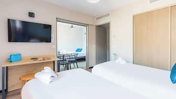 A hotel room with two beds, a desk with a chair, a TV mounted on the wall, and a wardrobe.