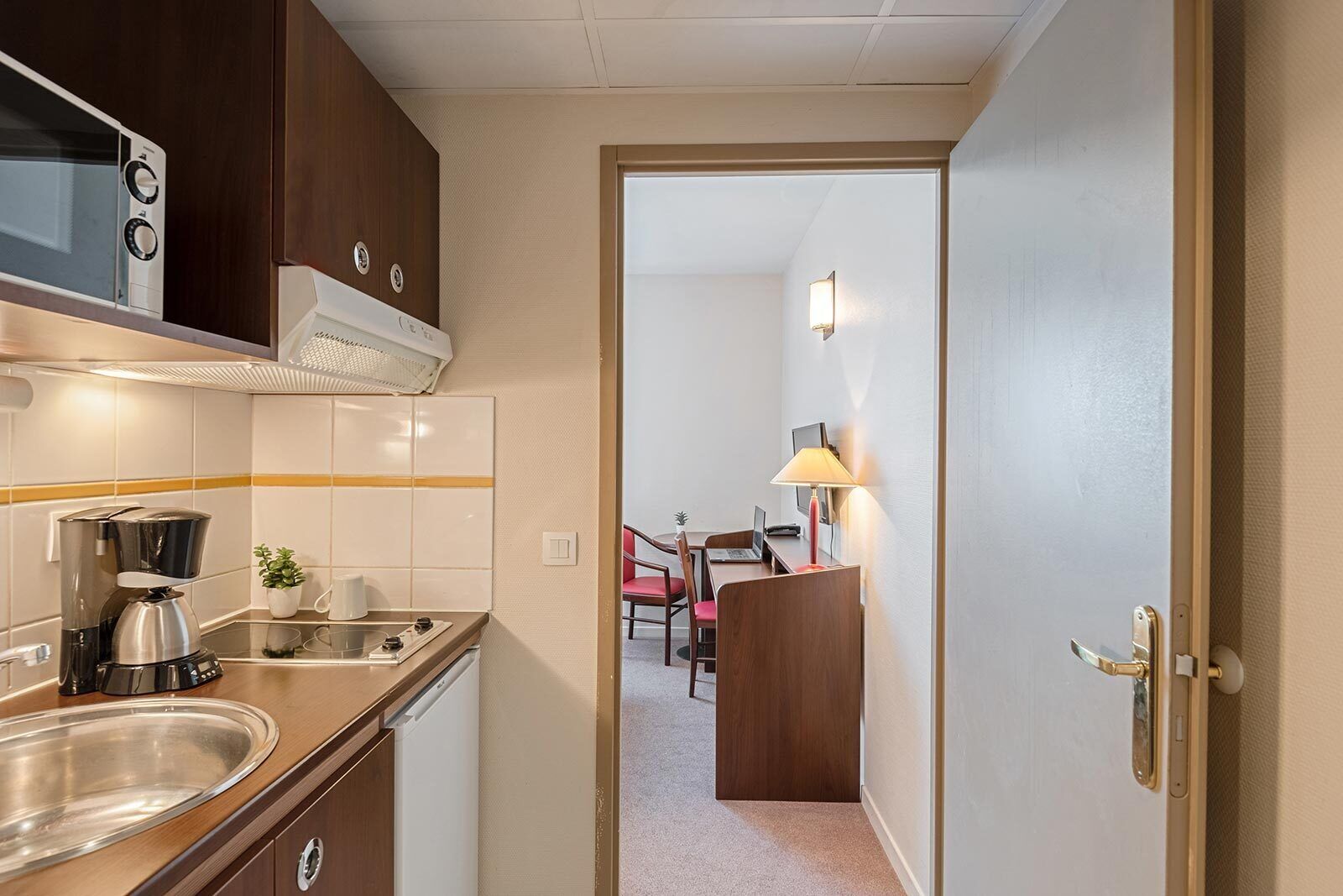 A compact kitchenette with a stove, sink, and microwave. A dining area with a table and chairs is visible in the background.