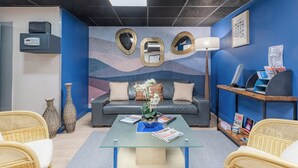 A modern room with a sofa, two wicker chairs, a glass coffee table, and a blue accent wall with abstract art. - Appart'City Classic Montélimar (Montélimar)