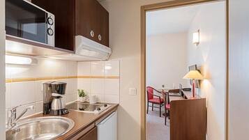 A compact kitchenette with a microwave, coffee maker, and sink. There is a dining area with a table and chairs visible through an open doorway.