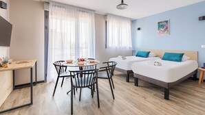 A modern hotel room with a dining area, two beds, a TV, and a poster on the wall. - Appart'City Classic Montélimar (Montélimar)