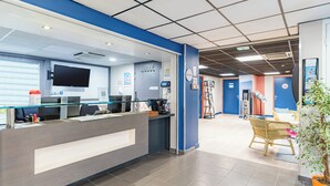 A reception area with a glass counter, a flat-screen TV, and a digital kiosk. - Appart'City Classic Montélimar (Montélimar)