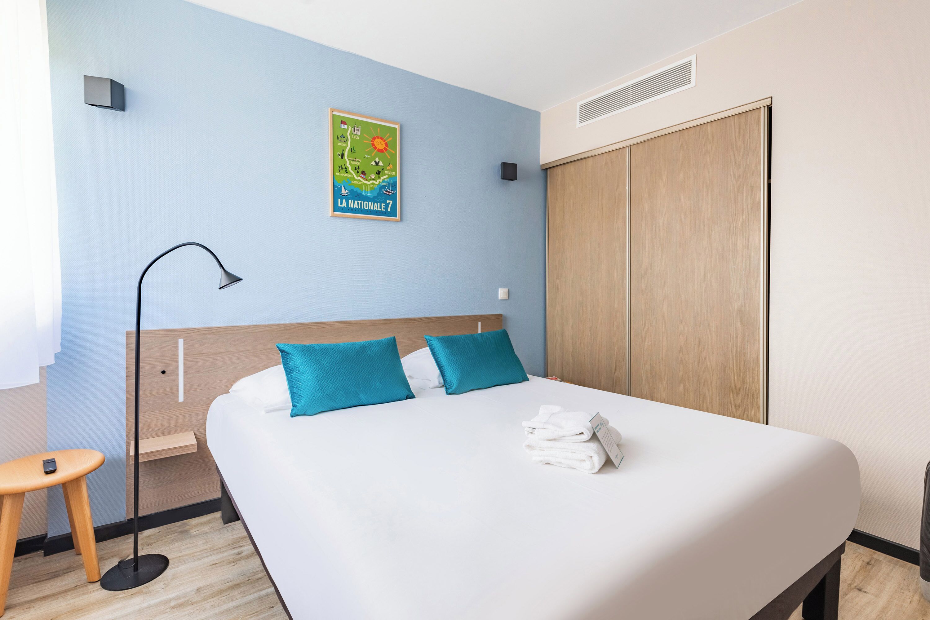 A neatly made bed with blue pillows, a bedside table with a lamp, and a map on the wall.