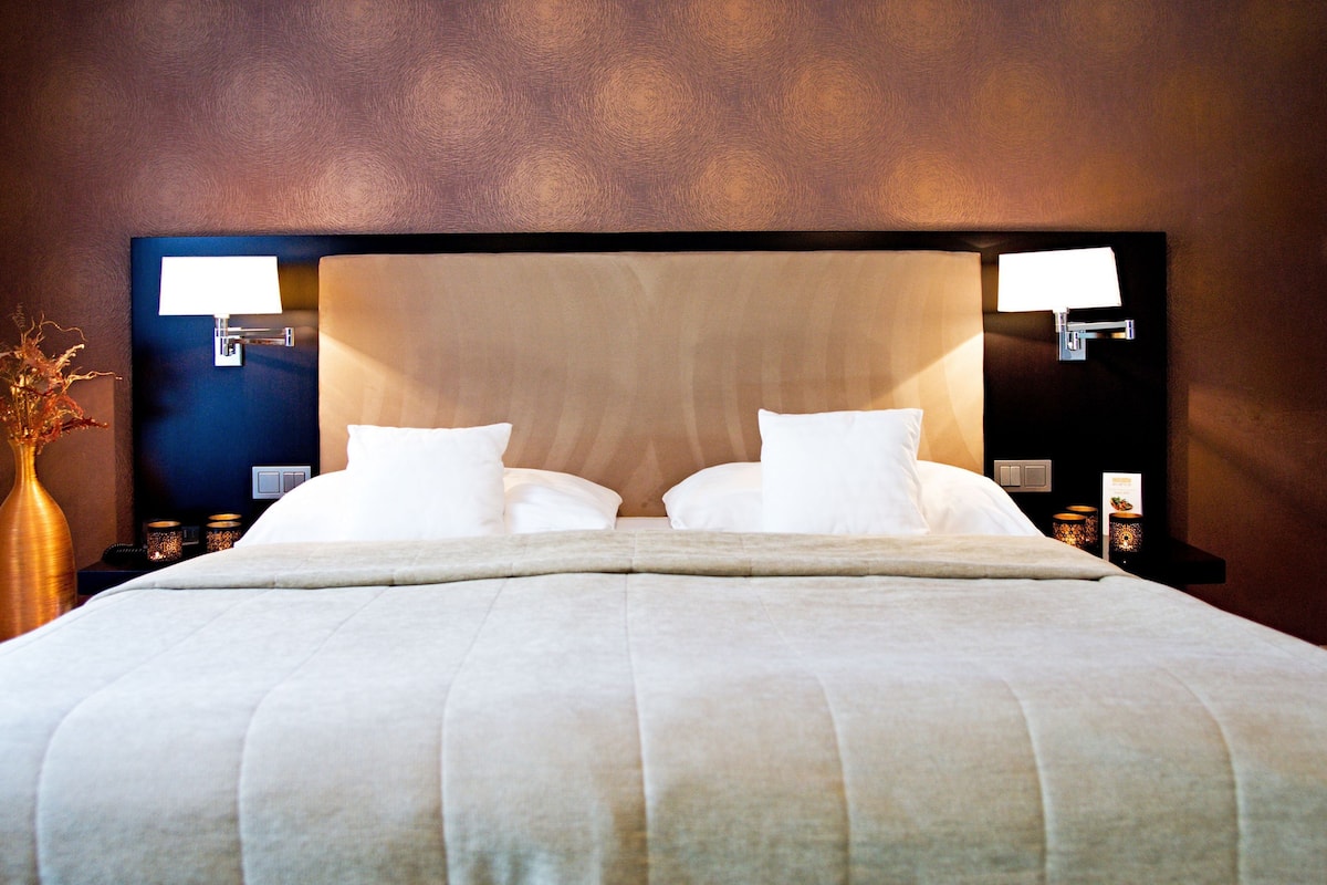 A double bed with a headboard, two bedside tables with lamps, and a vase with dried flowers on the left side.