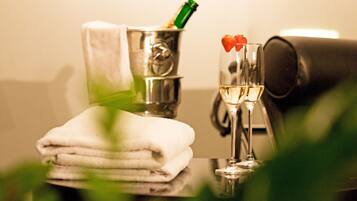 A bottle of champagne, a glass with a strawberry garnish, and a stack of white towels on a reflective surface.
